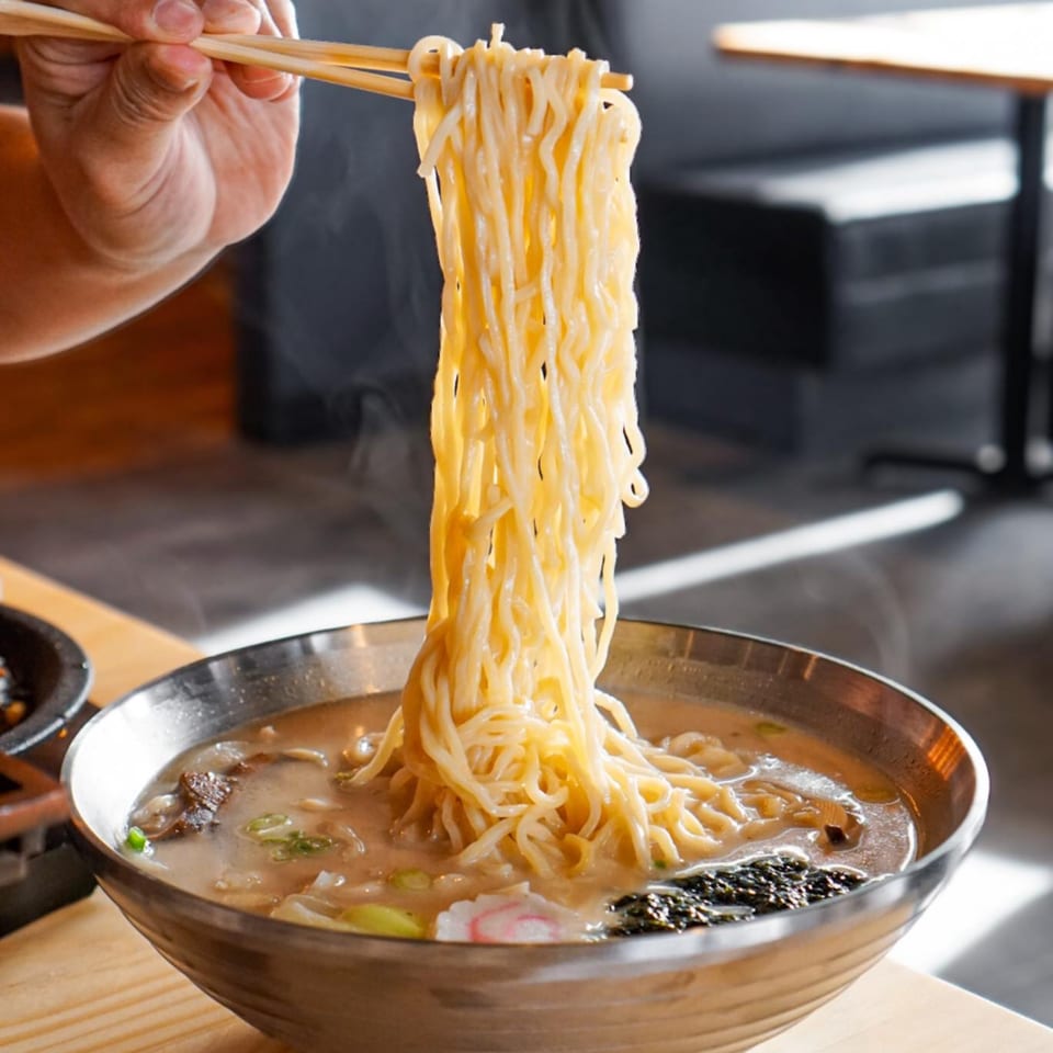 Chopsticks lift steaming noodles from a bowl of Taiwanese hot pot at Tasty Pot!