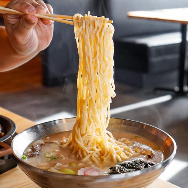 Chopsticks lifting steaming noodles from a Taiwanese hot pot with meat and vegetables.
