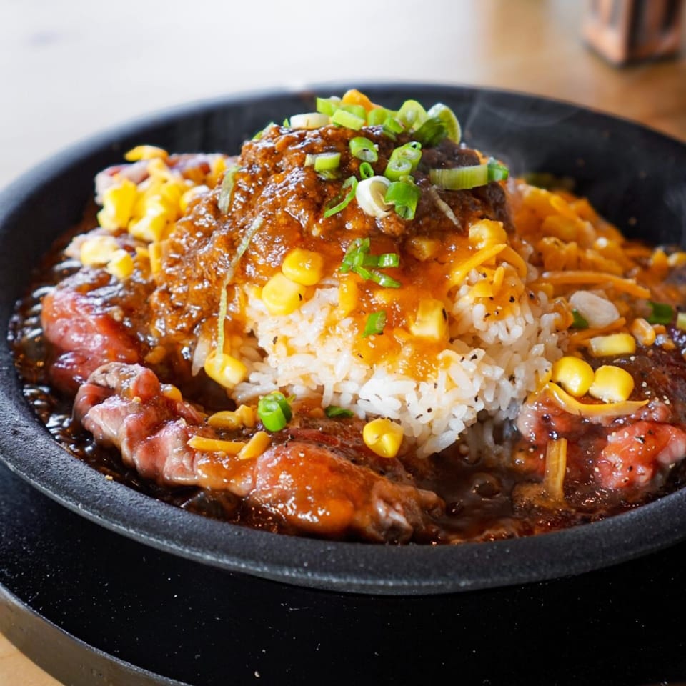 Sizzling Taiwanese hot pot with beef, rice, corn, cheese, and green onions in a black bowl.