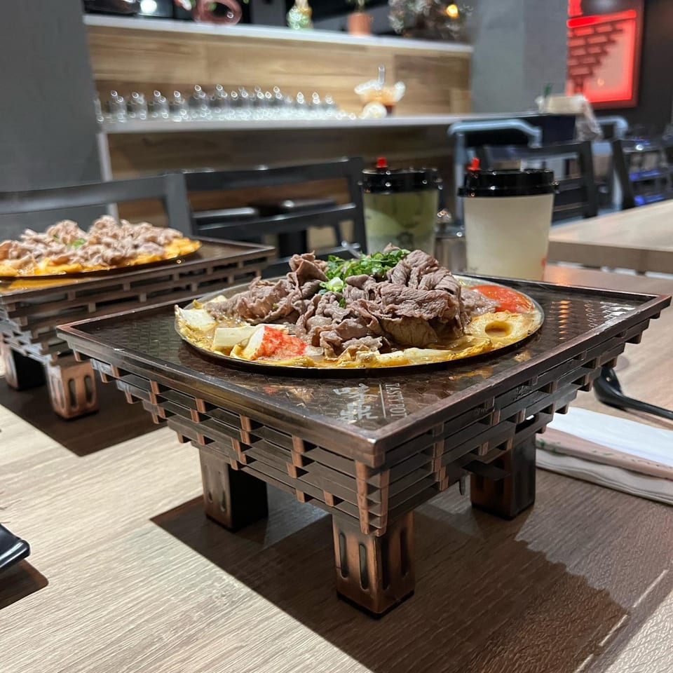 Two Taiwanese hot pots with beef, vegetables, and broth on wooden stands at Tasty Pot!