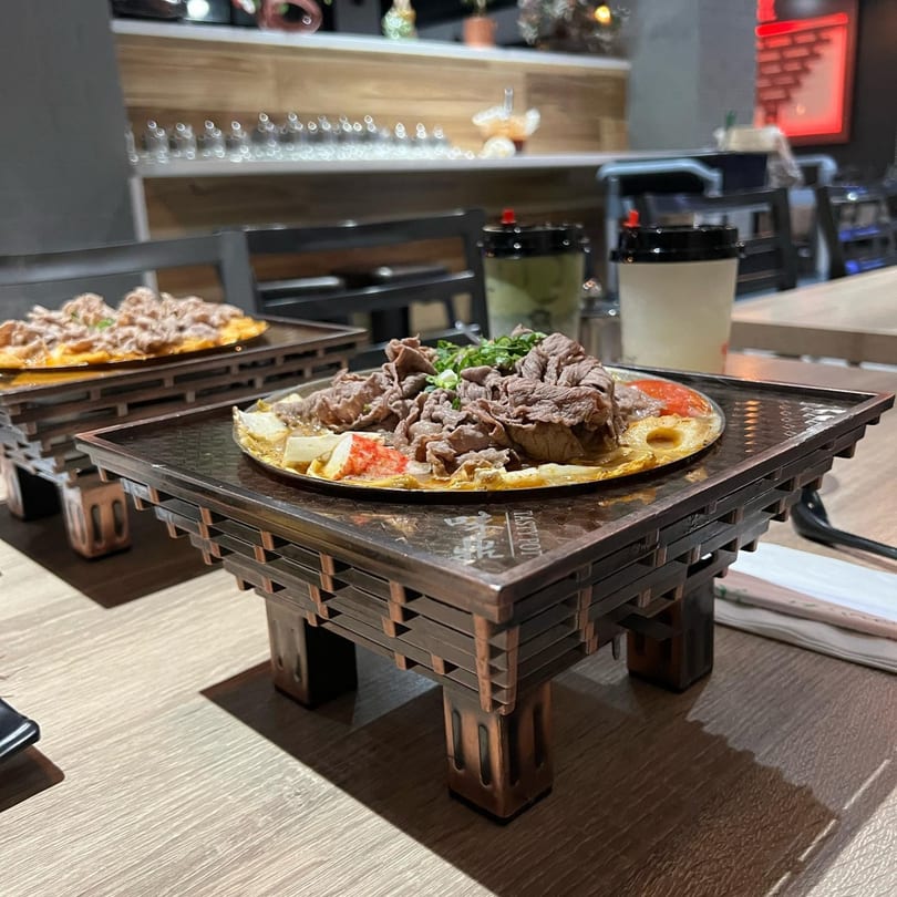 Two Taiwanese hot pots with beef, vegetables, and broth on wooden stands at Tasty Pot!