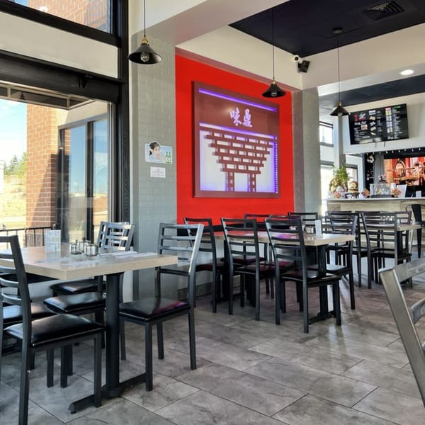 Interior of Tasty Pot! restaurant with empty tables, black chairs, and a red accent wall.