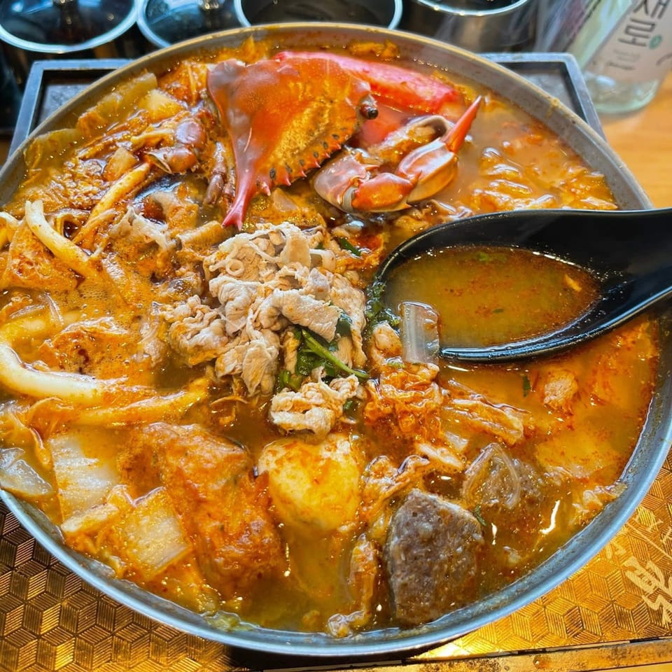 A bubbling Taiwanese hot pot with crab, sliced meat, and various ingredients in a rich broth.