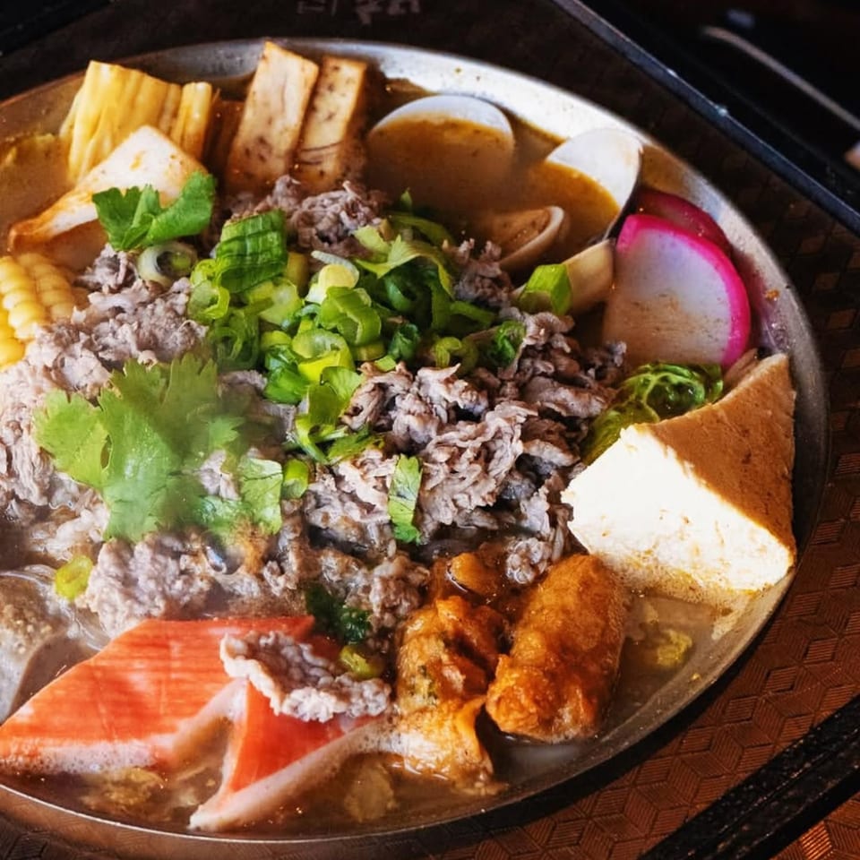 Close-up of a Taiwanese hot pot with beef, tofu, corn, crab, and various vegetables.