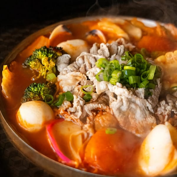 Steaming Taiwanese hot pot with sliced meat, broccoli, fish balls, and green onions in a rich broth.
