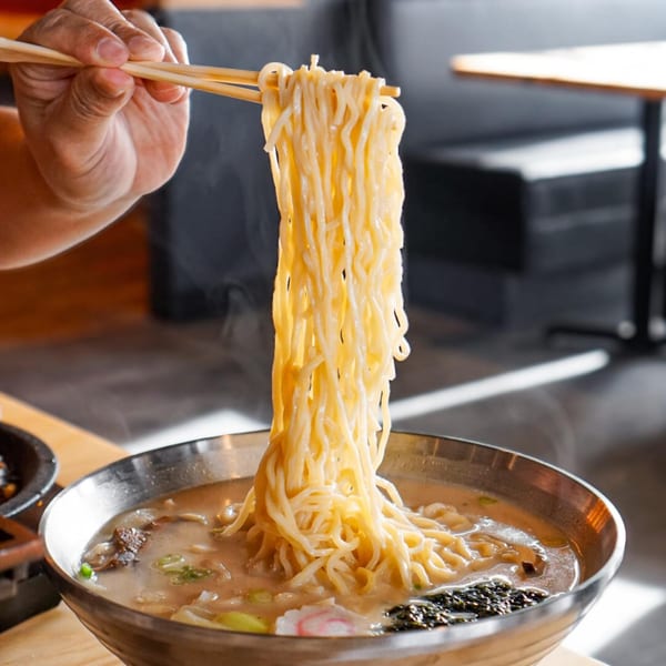 Chopsticks lifting steaming noodles from a Taiwanese hot pot at Tasty Pot!